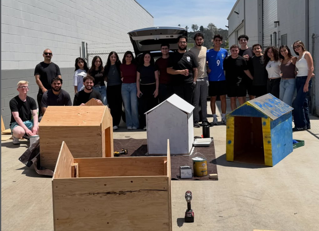 Project Archie volunteers standing together behind the doghouses they built