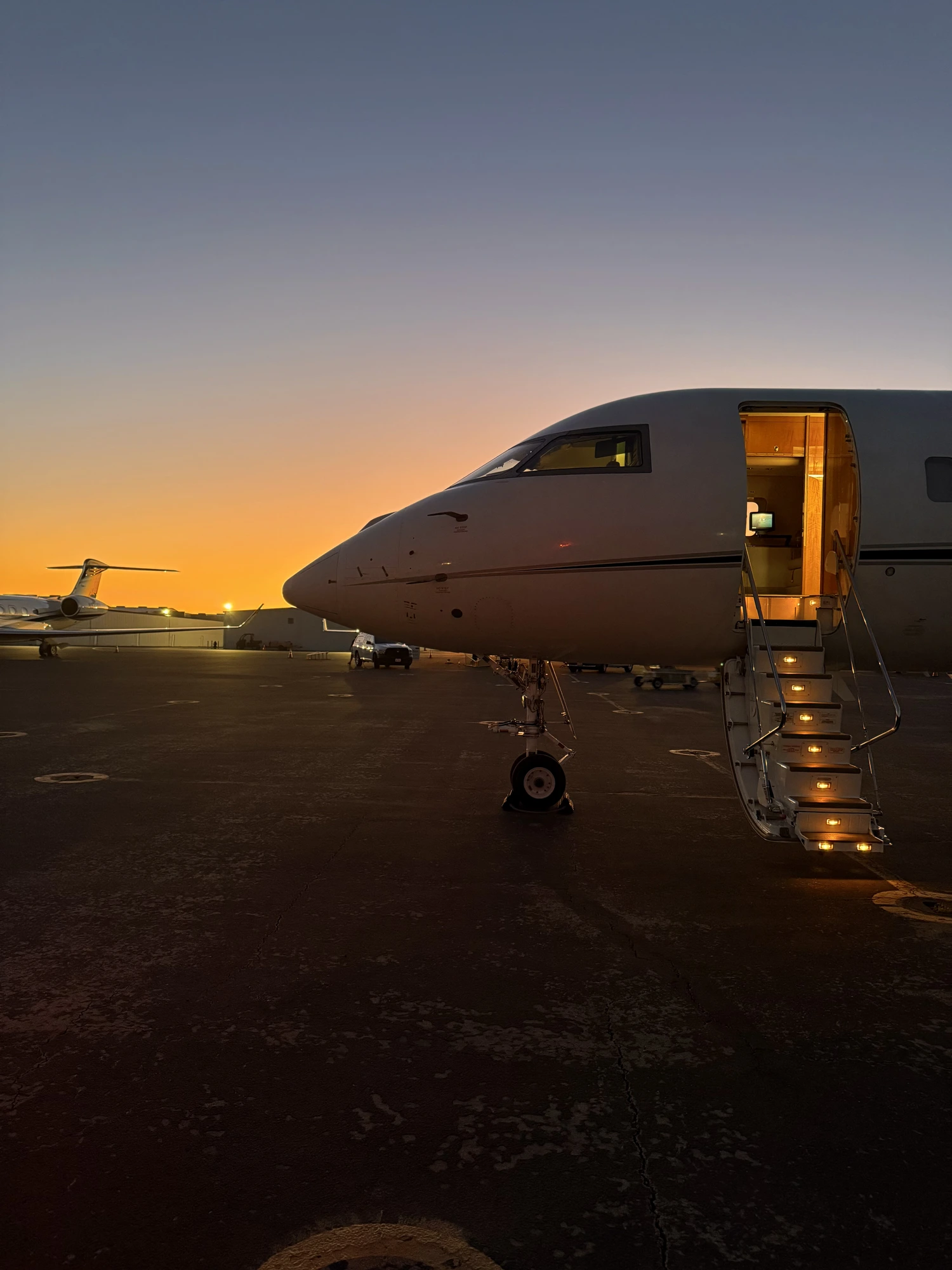 Private jet at sunset on the ramp, cabin door open with stair lights on.