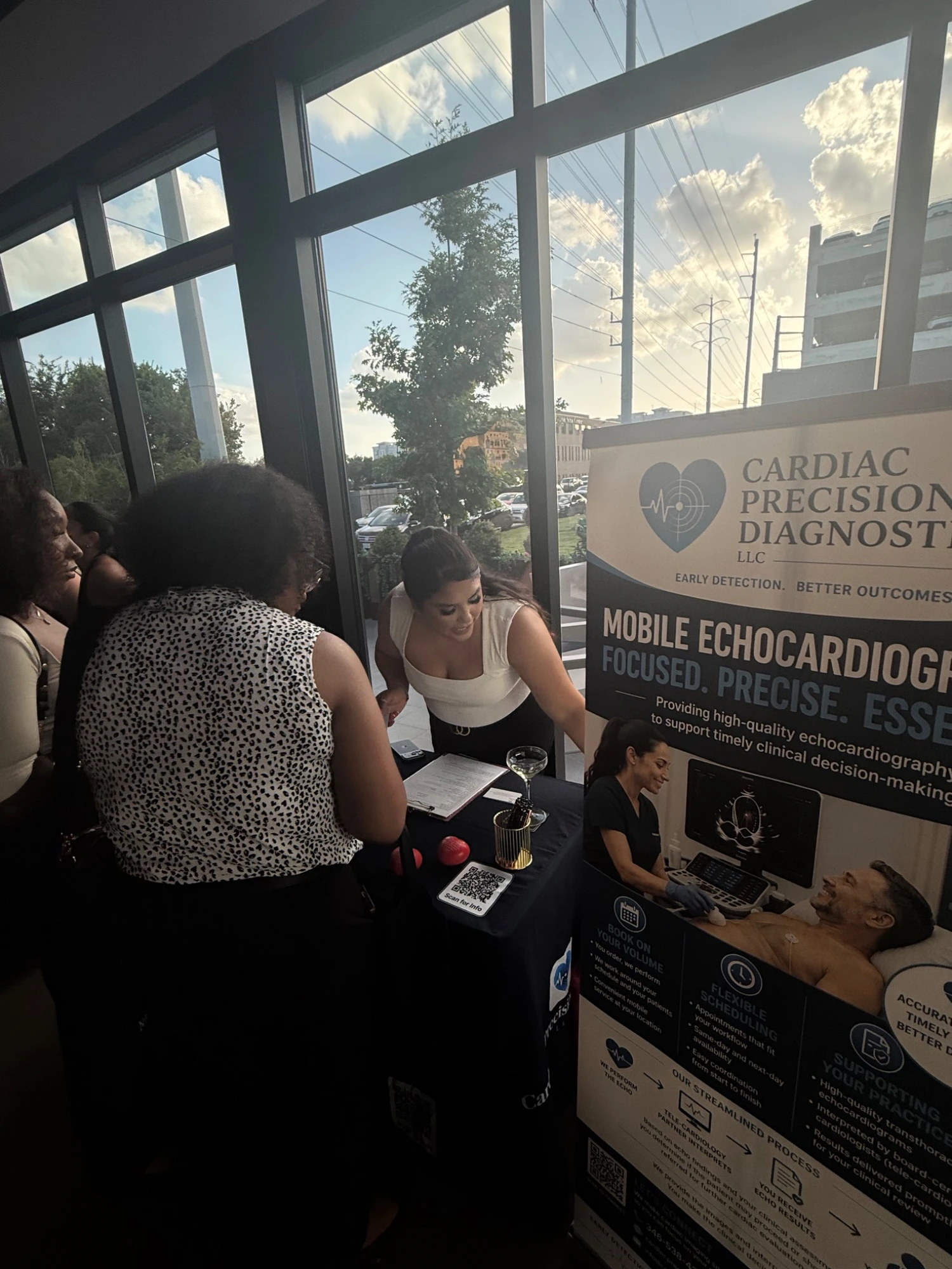 A Cardiac Precision Diagnostics representative engaging with attendees at a community heart-health outreach event, beside the CPD banner.