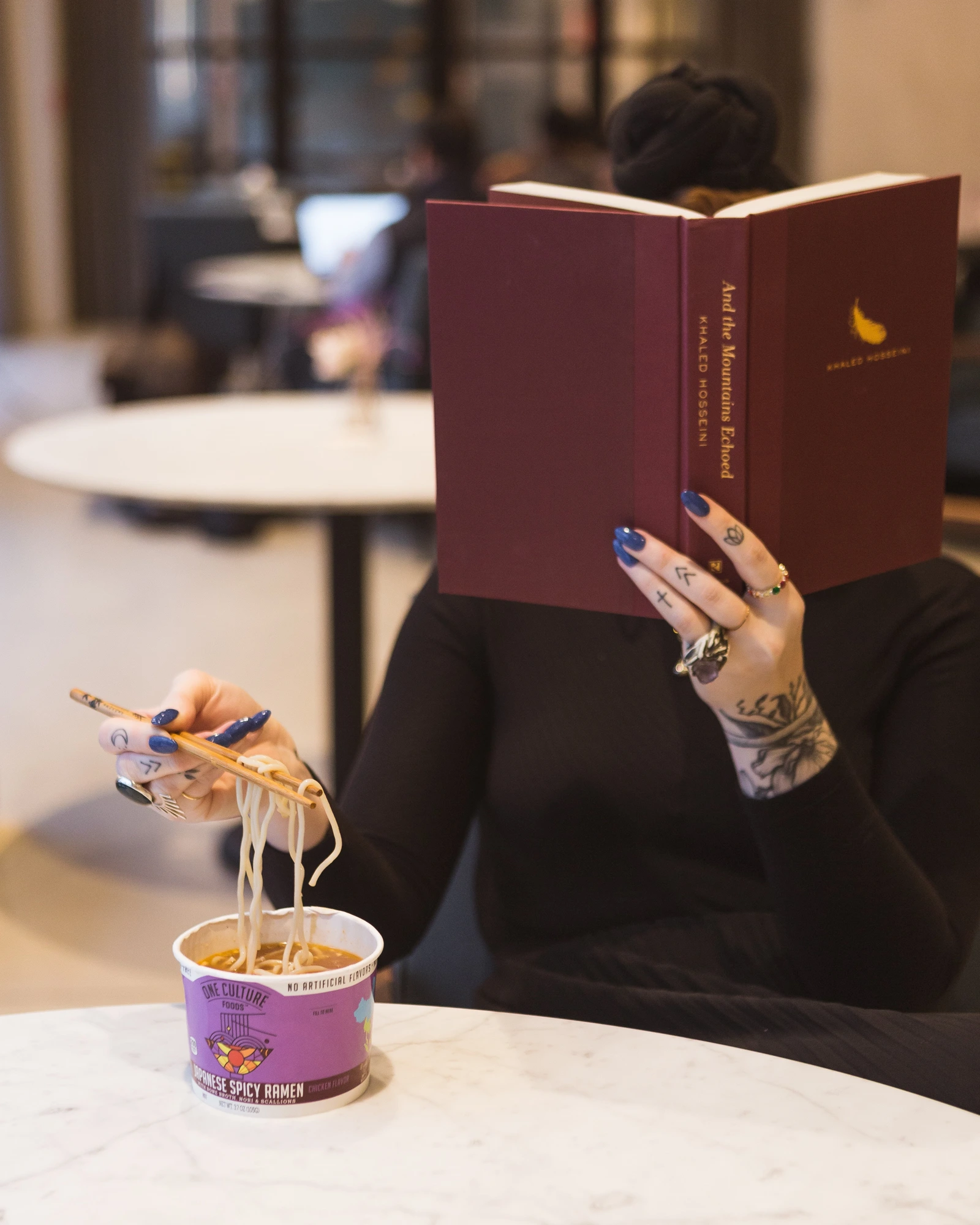 A student reading a novel over a cup of ramen — a quiet moment of college life